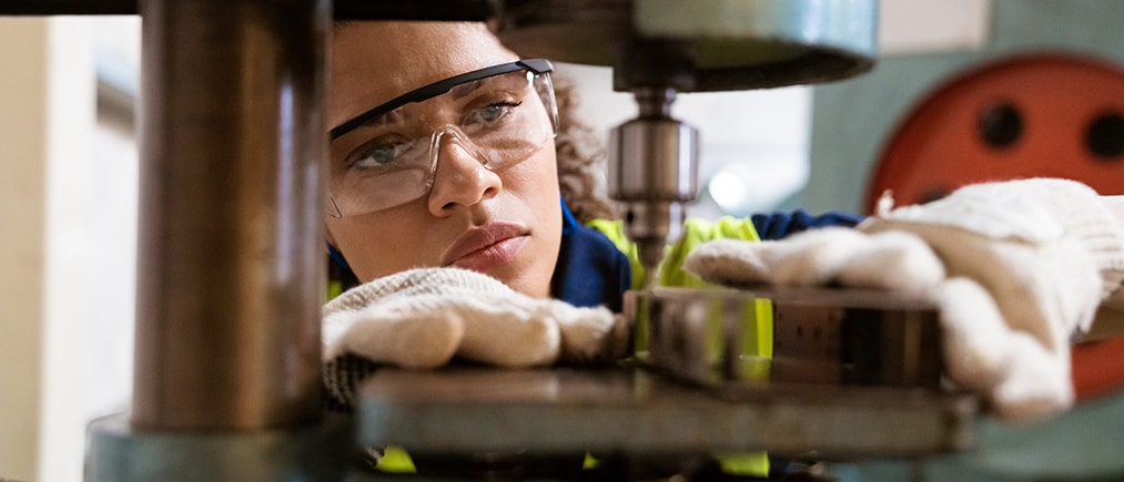 Close-up of female apprentice using yoke machine. Female engineer is wearing protective glasses in factory. She is working in manufacturing industry.